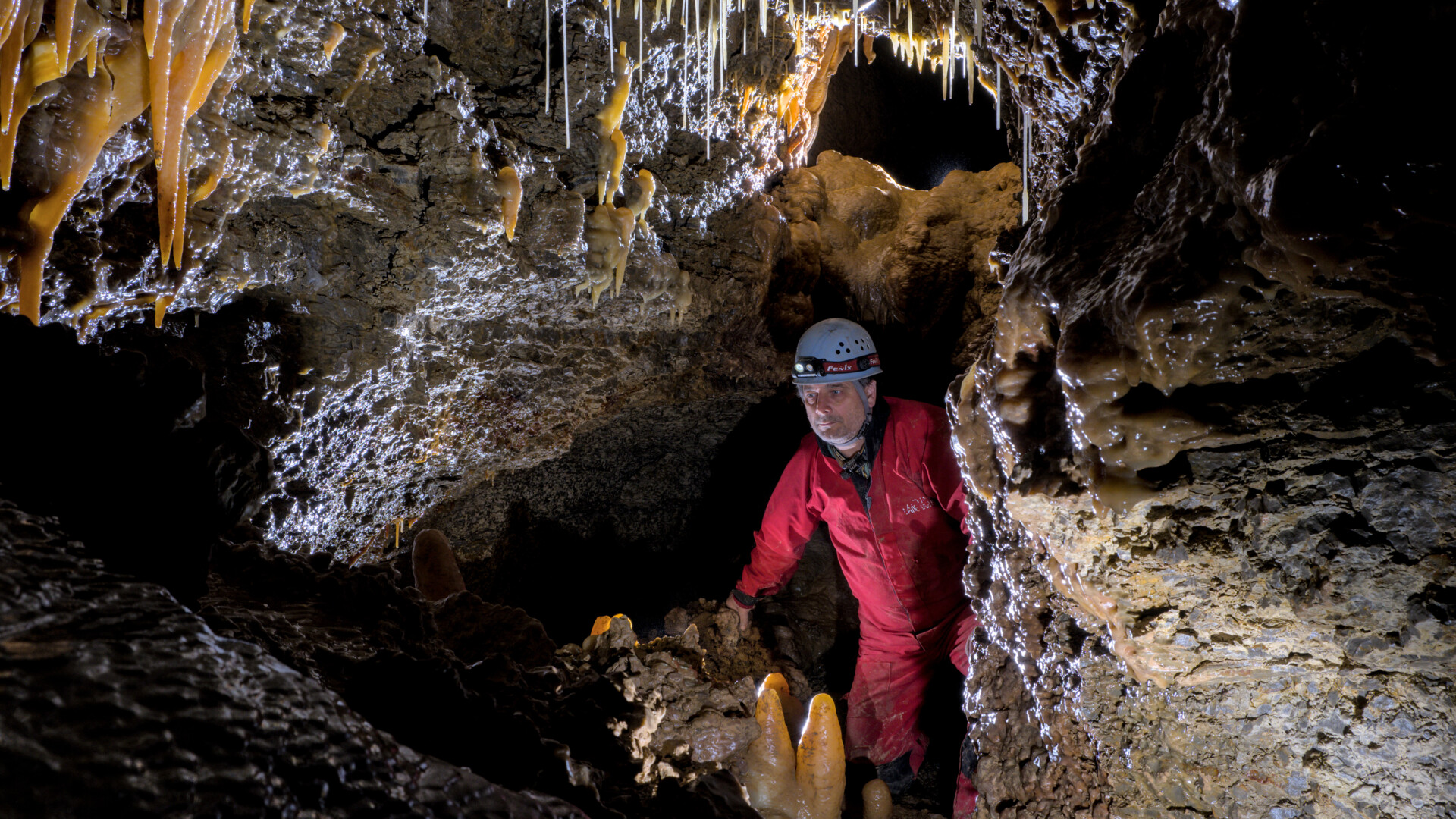 Bergmann Georg Schollän in rotem Schutzanzug und Helm mit Licht zwischen den Wänden der Bleßberghöhle (Alle Verwertungsrechte Thüringer Höhlenverein e.V.)