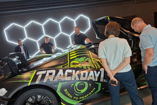 Besucher*innen des Jungunternehmer-Stammtisches stehen in den Räumlichkeiten bei Herzfahrer um die „Angry Fiona“, das Werbeauto von Trackday1
