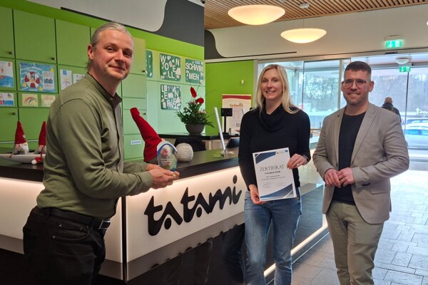 Platz 3 Top Akzeptanzstelle: Freizeitbad Tatami Severin Kühnast, Geschäftsführer der Schmöllner Stadtwerke, der einen kleinen Pokal hochhält, Julia Waldmann, Wirtschaftsförderin, die ein Zertifikat hochhält, und Bürgermeister Sven Schrade stehen an der Rezeption im Eingangsbereich des Tatami