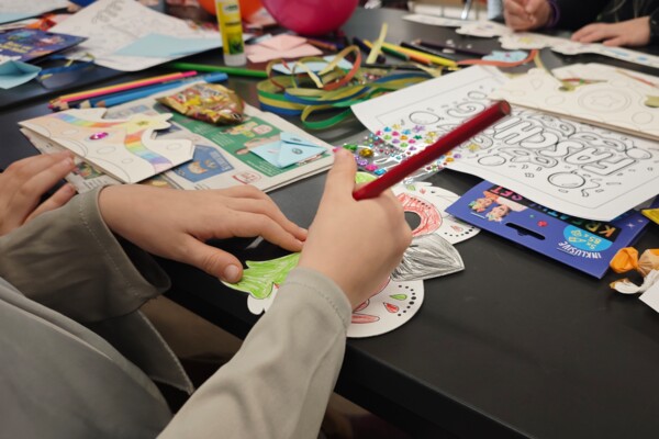 Detailaufnahme Hand beim Basteln Detailaufnahme auf den Tisch beim Faschingsbasteln in der Schmöllner Bibliothek auf Kinderhände, die gerade eine Eulenmaske bunt ausmalen