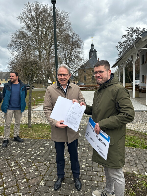 Bild mit Thüringens Innenminister Georg Maier, der dem Schmöllner Bürgermeister Sven Schrade den Scheck mit der Prämie für die Eingliederung Dobitschens auf dem Dorfplatz überreicht