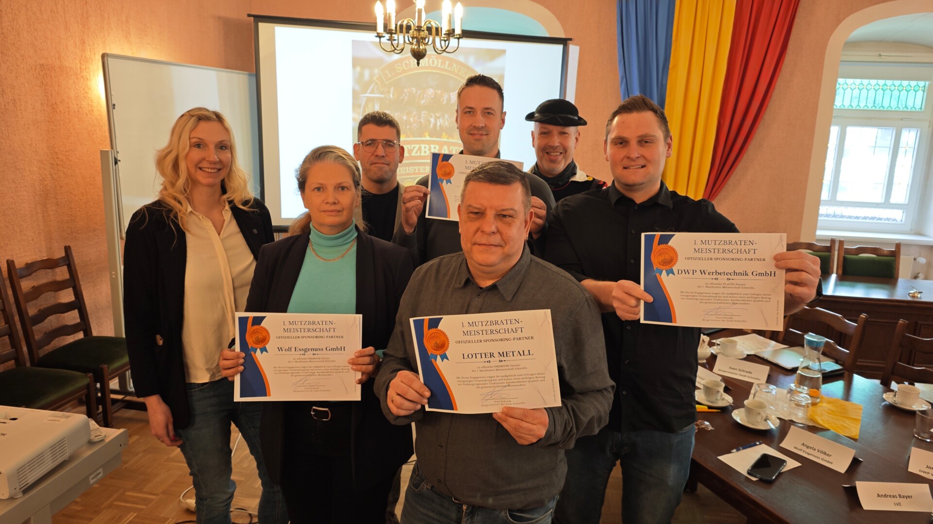 Gruppenfoto aller Sponsoren der 1. Mutzbraten-Meisterschaft mit dem Bürgermeister Sven Schrade, der Wirtschaftsförderin Julia Waldmann und einem Mann in Tracht im Ratssaal zur Besprechung der Meisterschaft