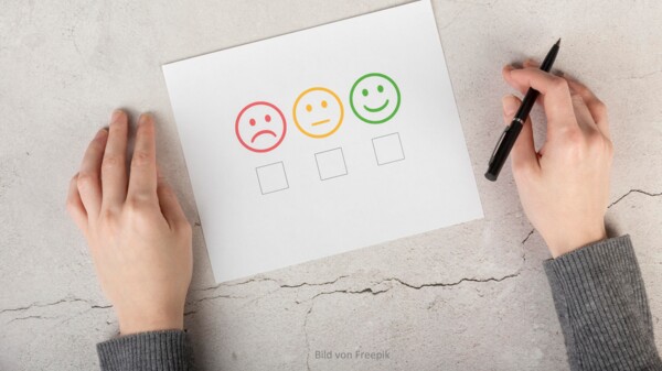 Bild Befragung - Hände mit Stft und drei bunten Smileys zum Abstimmen