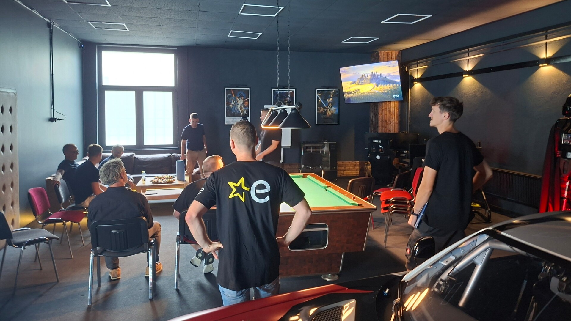 Blick in die Räumlichkeiten bei Herzfahrer auf die Besucher*innen des Jungunternehmer-Stammtisches, die um einen Billard-Tisch verteilt stehen und sitzen