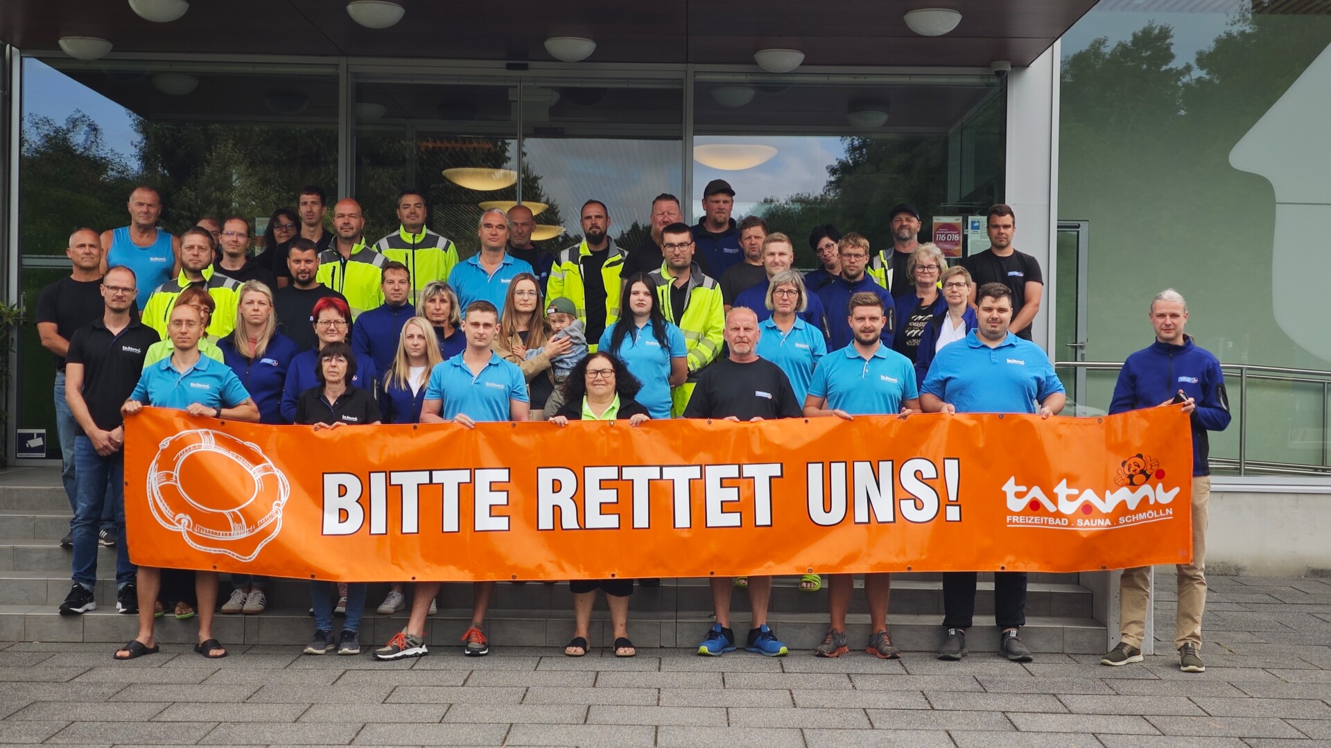 Gruppenbild: Alle Tatami-Mitarbeiter vor dem Haupteingang - mit Banner in der Hand